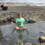 boy doing yoga in a rockpool by the sea